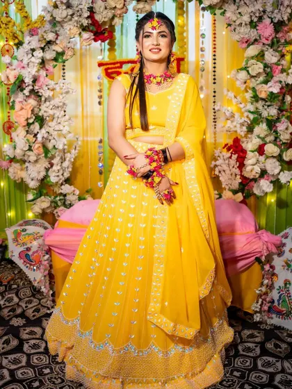 Another beautiful shot of the bride in her yellow Haldi outfit, perfectly complemented by the floral decor in the background.