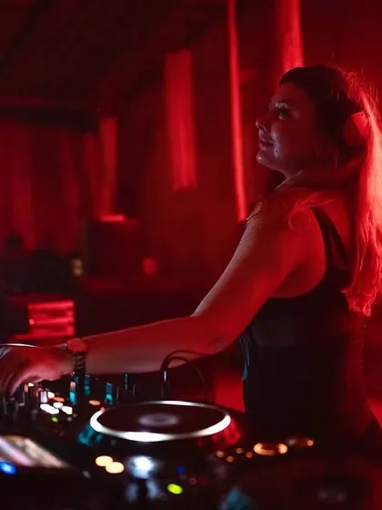 In the red-lit DJ booth at Aura, focused on the mix. The neon lights create a classic club vibe.
