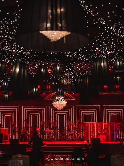 A stage designed to steal the spotlight under an indoor night sky. The combination of a starry ceiling, dramatic red geometric lighting, and crystal chandeliers created a magical and moody setting for the sangeet performances.
