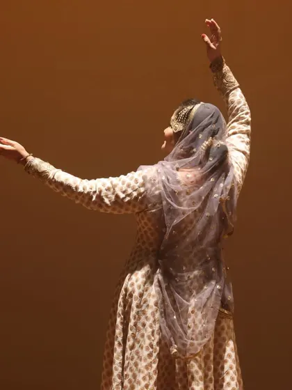 The back view of a Kathak dancer, highlighting the elegant costume and graceful arm gestures that are integral to the performance.