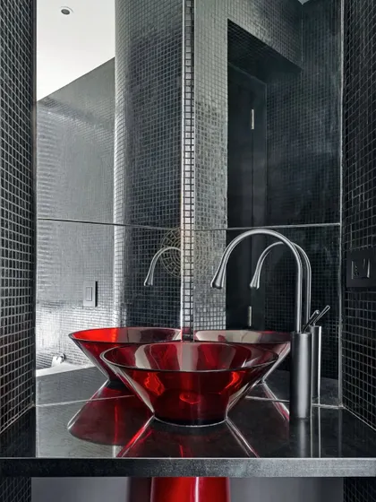 This powder room makes a bold statement with black mosaic tiles and a vibrant red acrylic basin. The reflection in the mirror amplifies the dramatic effect of the contrasting colors.