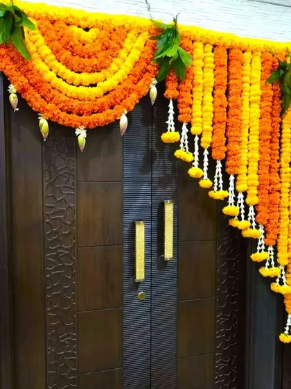 A traditional Griha Pravesh decoration for a main door. The arch is made of marigold garlands with hanging bell and leaf accents.
