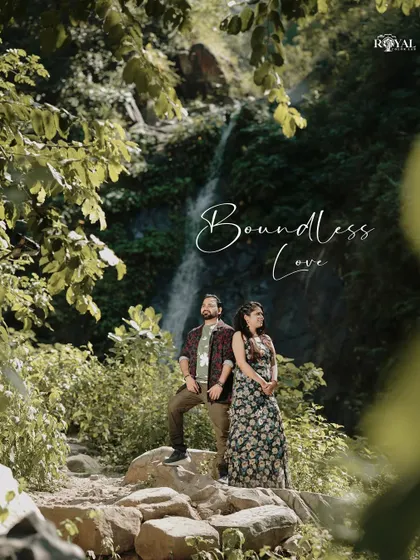 A stunning wide shot of a couple standing on rocks in a lush forest, with a waterfall in the background, titled 'Boundless Love'.