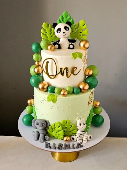A chic and modern jungle-themed cake for a first birthday. This design uses a clean white and green palette with gold accents, and features cute panda, elephant, and zebra toppers.