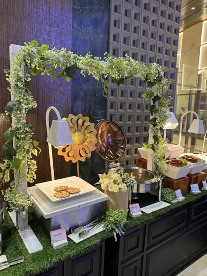 A fresh and airy buffet station framed by an arch of white and green foliage. This design brings a touch of nature indoors, creating a refreshing and vibrant atmosphere for daytime corporate events.