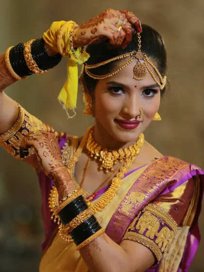 A South Indian bride adjusting her hair, showcasing her beautiful gold jewelry, henna, and traditional silk saree.