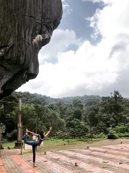 A graceful Natarajasana, or dancer's pose, practiced in the open space before a unique, face-like rock formation in Yana.