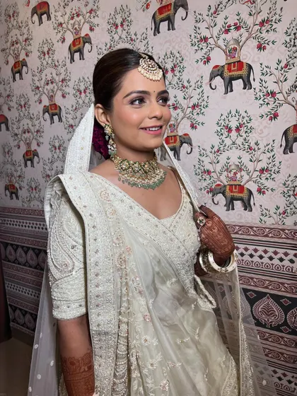 A happy bride in her elegant white ensemble. The makeup is subtle yet defining, with a focus on the eyes and a natural lip color.
