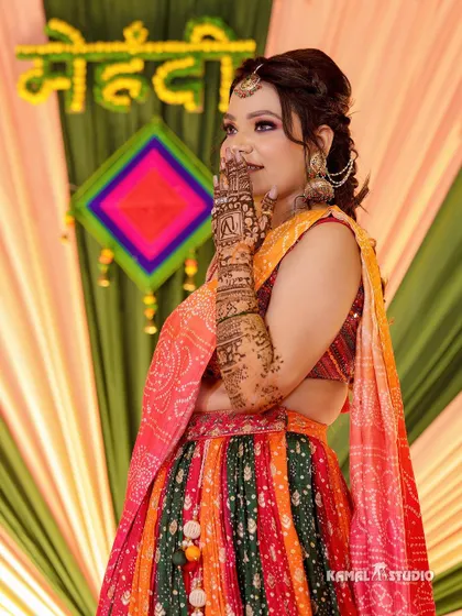 The bride posing in front of a vibrant "Mehendi" backdrop, showing off her henna.