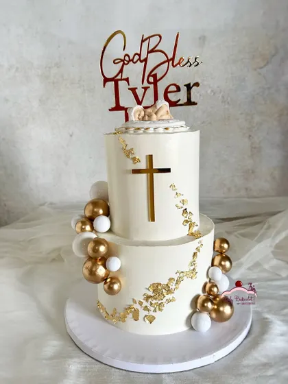 A two-tier baptism cake for baby Tyler. The design is clean and elegant, with white and gold accents and a cross cutout.