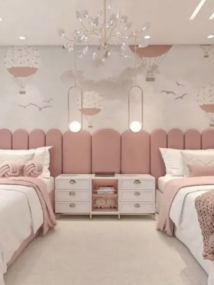 This shared girls' room is designed with a lovely pink palette and a hot air balloon themed wallpaper. The long, scalloped headboard unifies the two beds, and the elegant chandelier adds a touch of glamour.