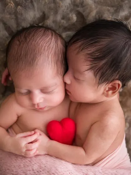Sharing a heart from the very beginning. This pose with the tiny red heart symbolizes the inseparable bond between these newborn twins.