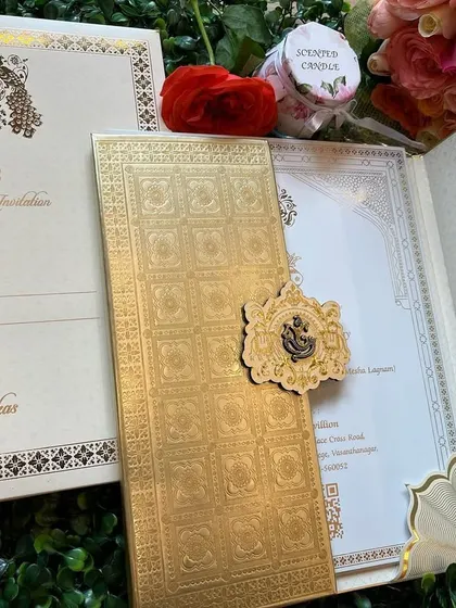 A truly royal invitation in off-white and gold. This card features a custom peacock crest, a Ganesha emblem, and an ornate clasp, all signifying opulence and tradition.