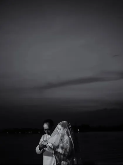 A dramatic black and white shot of the bride and her father against the dark sky and water in Kashmir, a powerful and moody portrait.
