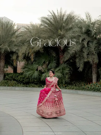 A graceful portrait of the bride in her pink lehenga, set against a backdrop of palm trees. The image is titled "Gracious," which she truly is.