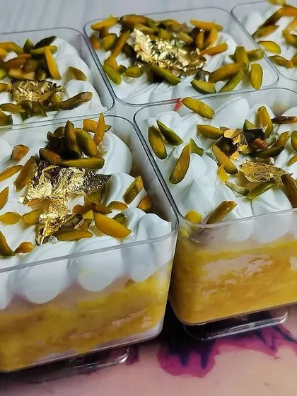 A detailed shot of the Kesar Pista Tres Leches Cups, focusing on the texture of the cream and the shimmer of the edible gold leaf.