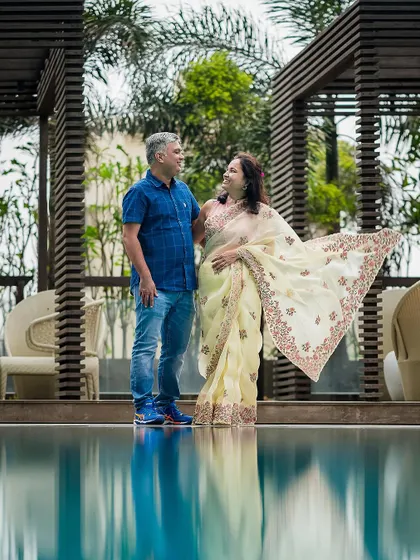 A couple stands by the pool, their reflection captured in the calm water. This setting provides a serene and elegant backdrop for an anniversary shoot.