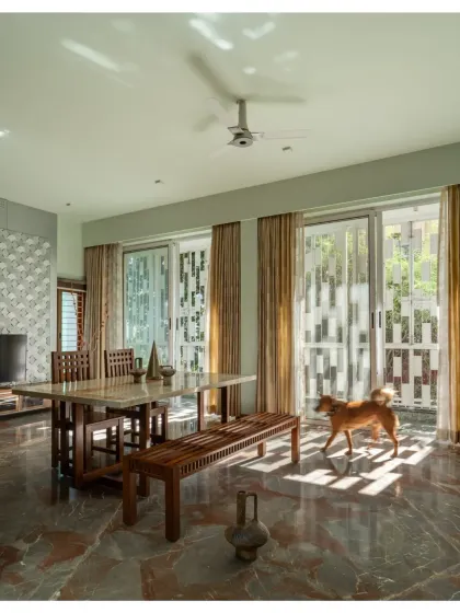 The dining area in the Shivom residence is filled with morning light, filtered through patterned screens that create a beautiful play of shadows on the marble floor.