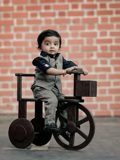 A handsome little boy on his wooden tractor, looking very dapper in his vest and bow tie.