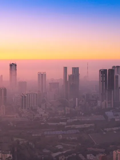 A closer view of Mumbai's skyscrapers piercing through the dense sunset haze, creating a layered and atmospheric cityscape.