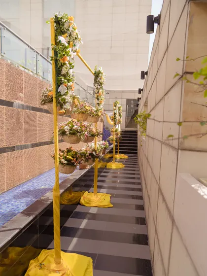 A floral aisle created with yellow stands holding baskets of fresh flowers, guiding guests along a poolside walkway.