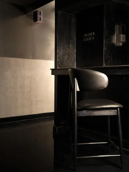 The bar area at Lair, a composition of shadow and minimal light. The design uses focused lighting to highlight the bottles and the dark, fluted bar front, creating a dramatic focal point.
