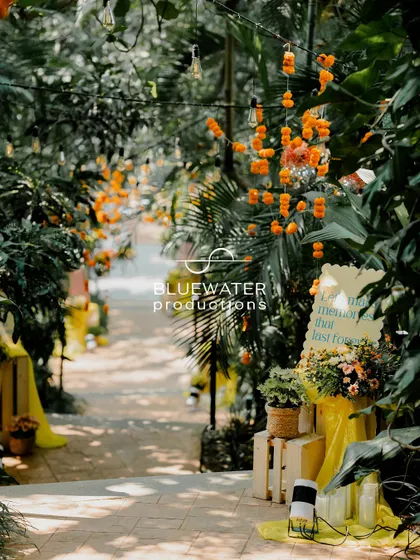 A pathway through the garden venue, lined with marigold strings and small floral arrangements, guiding guests to the celebration.
