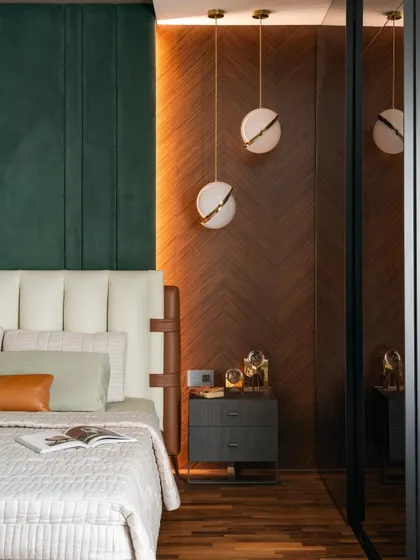 This master bedroom combines a plush green headboard with a chevron-patterned timber wall. Spherical pendant lights add a sculptural touch to the serene space.
