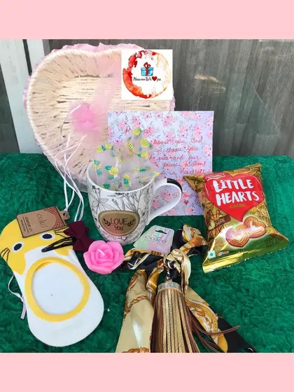 A heart-shaped basket filled with Valentine's treats, including a "Love You" mug, Little Hearts biscuits, and a cute eye mask.