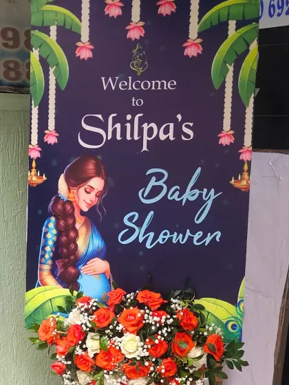 A traditional welcome banner for Shilpa's baby shower, featuring classic Indian art and decorated with fresh orange roses.