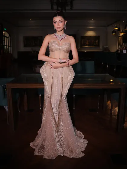 A full view of the champagne silk gown, showcasing its sculpted peplum details and the delicate, shimmering handwork on the fish-cut skirt.