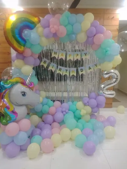 A dreamy unicorn-themed decoration for a 2nd birthday. We used a pastel rainbow balloon arch, a silver fringe curtain, and large unicorn and rainbow foil balloons to create a magical party space.