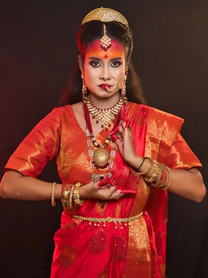 A student's portrayal of Maa Katyayani, the warrior goddess. The makeup is strong and fierce, with an emphasis on the eyes and traditional red and orange hues.