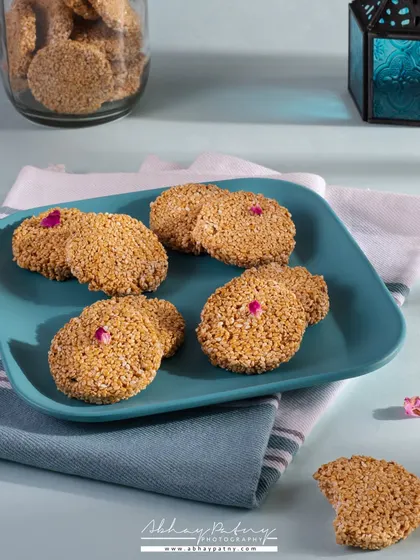 This image of Gajak (sesame brittle) is styled with a cool blue plate and a lantern prop to evoke the feeling of a winter evening, which is when this sweet is traditionally enjoyed.