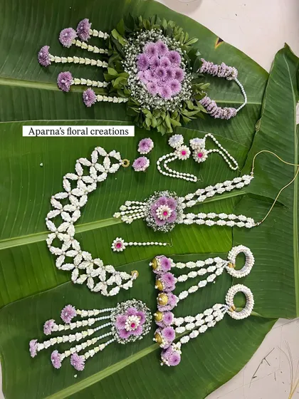 This flat lay shows a complete floral jewellery set in purple and white, crafted for a baby shower. It includes a choker, long necklace, bajuband, and hair accessories.