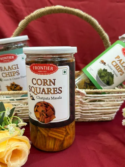 A close-up of the healthy snacks we include in our wedding hampers. This basket features Frontier's Corn Squares, Ragi Chips, and Palak Chips, offering a tasty and wholesome treat for guests.
