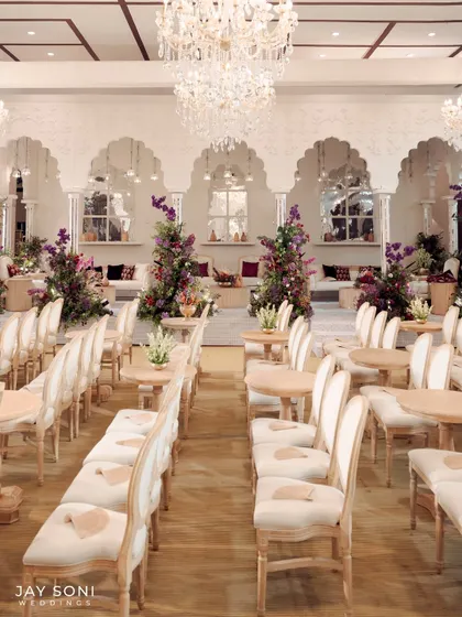 The main seating area for the ceremony, with rows of classic white chairs leading towards a beautifully decorated lounge space under magnificent chandeliers.