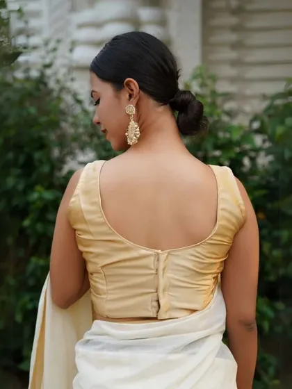 A model wears statement gold earrings that beautifully complement her simple, elegant gold blouse and white saree.