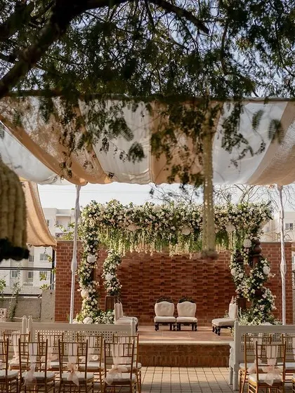 This perspective shot shows the beautiful floral mandap framed by the venue's trees and the striped canopy above, highlighting how the decor is integrated with the natural environment for a cohesive look.
