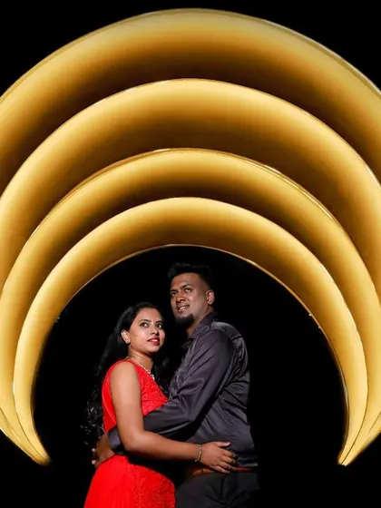 A couple poses under a modern, illuminated arch against a black background. The creative lighting makes for a striking and contemporary portrait.