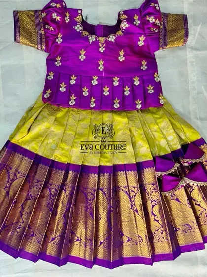 A flat-lay of a yellow and purple pattu pavadai. The purple peplum top has delicate white floral embroidery.