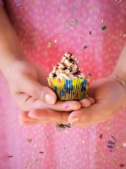 A festive cupcake held in two hands with confetti falling all around. This shot is full of joy and movement, perfect for a birthday or celebration-themed campaign.