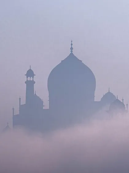 The silhouette of the Taj Mahal emerging from a thick layer of morning fog, creating a mysterious and ethereal scene. The Taj Mahal as you've rarely seen it. This photo, taken during a foggy winter morning in Agra, captures the monument's dreamlike quality, focusing on atmosphere over detail.