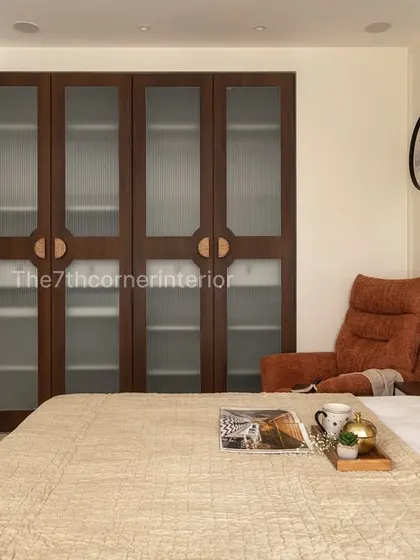 A view across the bedroom, highlighting the large wardrobe with dark wood framing and fluted glass panels. The design provides ample storage while maintaining the room's warm and inviting aesthetic.