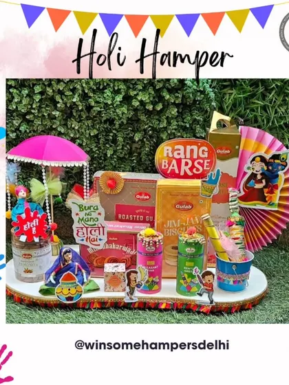 A delightful Holi hamper set against a green backdrop. This tray is filled with "Rang Barse" themed goodies, including snacks, thandai, and buttermilk, and decorated with a miniature umbrella and festive cutouts.