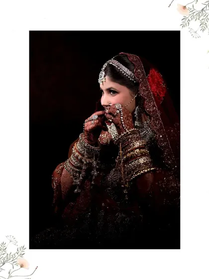 An artistic, low-key portrait of a bride in a red lehenga, her hands near her face, drawing attention to the intricate henna and jewelry.
