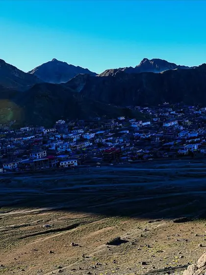 The early morning sun casts long shadows over a village nestled in the Ladakh valley, as seen from a high vantage point during a morning trek.