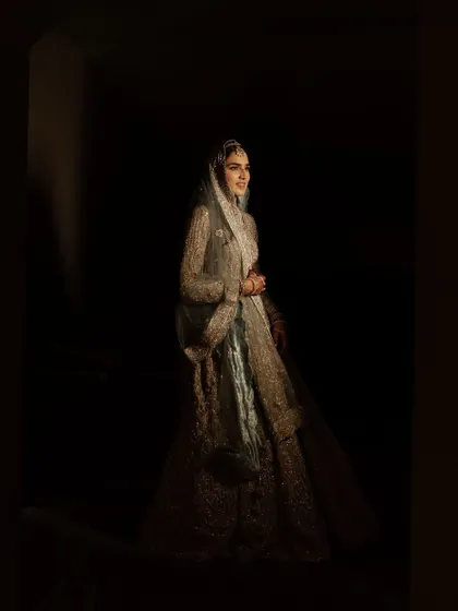 A full-length portrait using dramatic, low-key lighting. The bride emerges from the shadows, creating a powerful and theatrical image that feels timeless.