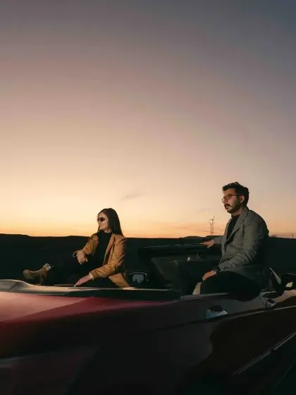 A beautiful wide shot of the couple in their convertible against the twilight sky, capturing the peaceful end to a day of shooting.