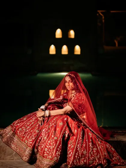 A stunning full-length portrait of the bride in her royal red lehenga, seated like a queen.